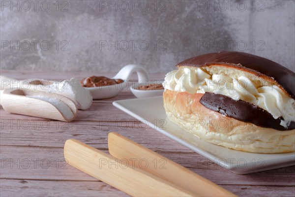 Delicious chocolate-covered cream eclair and white ceramic spoons with chocolate and cocoa on the side with wooden tongs