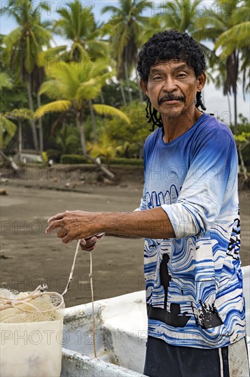 Man looking at the camera preparing his net to fish in his boat with palm trees in the background