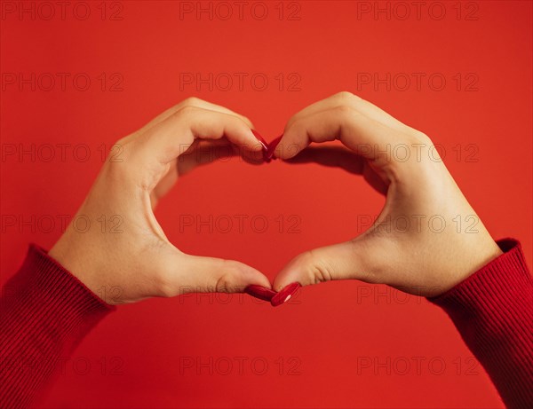 Female hands make a heart shape. Hands of a young white girl with a beautiful bright red manicure. Close up. Valentine day concept. Red background