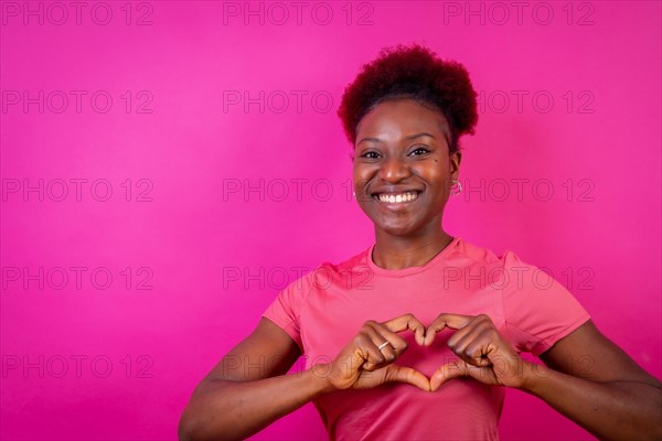 Young african american woman isolated on a pink background smiling and heart gesture