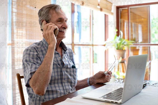 Mature business man smiling and talking on phone in front of laptop