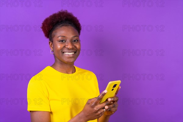 Young african american woman isolated on a purple background smiling with the mobile phone