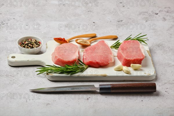 Three uncooked pork cutlets on white cutting board