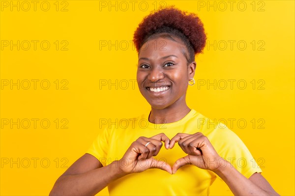 Young african american woman isolated on a yellow background smiling and heart gesture