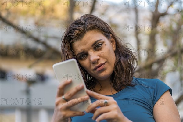 A beautiful latin woman using her smartphone outdoors looking at camera