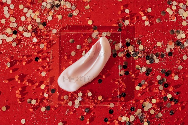 Cosmetic smear of white cream on transperent glass. Bright red background with silver glitters and confetti. Concept of health and celebration. Copy space
