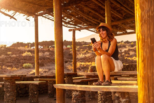 A woman tourist at sunset with the mobile smiling on the beach of Tacoron on El Hierro