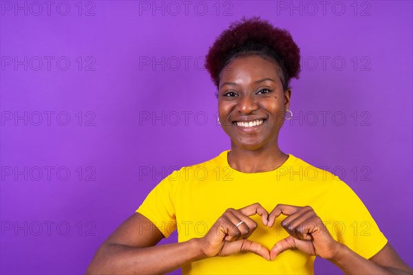 Young african american woman isolated on a purple background smiling and heart gesture