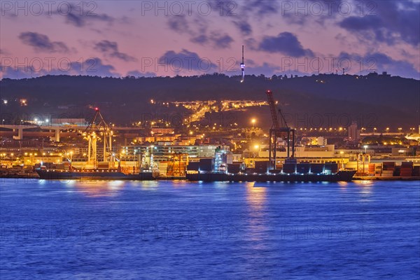 View of Lisbon port with sea container ships with port cranes in the evening twilight over Tagus river. Lisbon