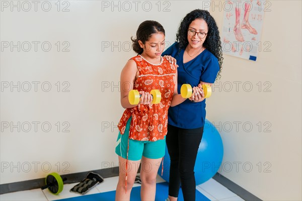 Physiotherapist assisting female patient with dumbbells on rehab ball. Rehabilitation physiotherapy with dumbbells