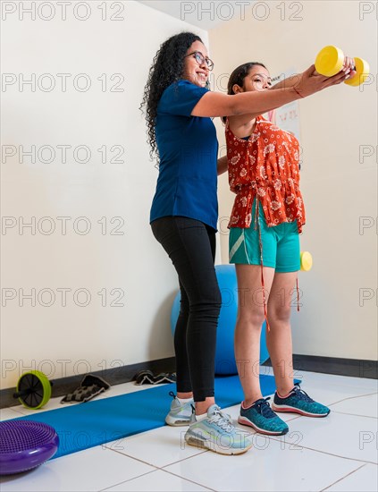 Rehabilitation physiotherapy with dumbbells. Physiotherapist helping patient with dumbbells on rehabilitation ball