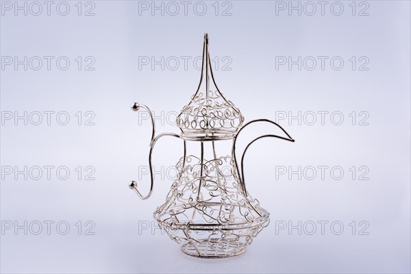 Silver color metal jug over a glass on a white background