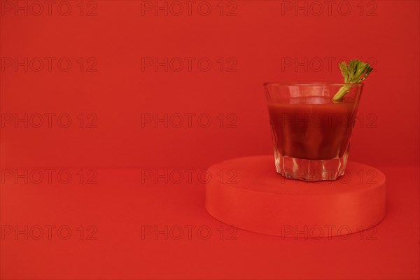 A glass of red cocktail with greens on the podium. Stylish alcohol tomato beverage Bloody Mary on a red background. Delicious drinks concept. Copy space