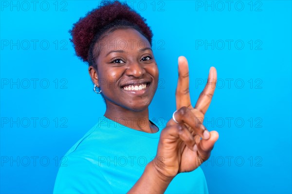 Young african american woman isolated on a blue background smiling with the victory gesture