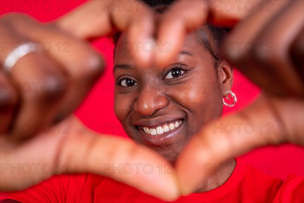Young african american woman isolated on a red background smiling and heart gesture
