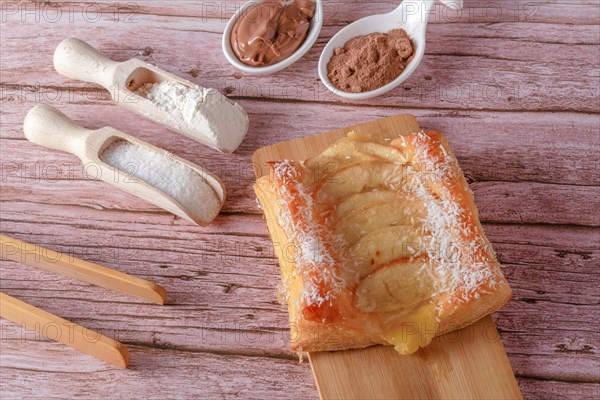 Top view apple pie with grated coconut on a wooden board spoons with chocolate