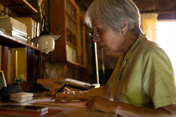 Serious mature woman in glasses thoughtful focused senior writing a letter at home