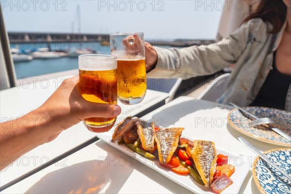 A couple toasting with beer by the sea eating fried fish
