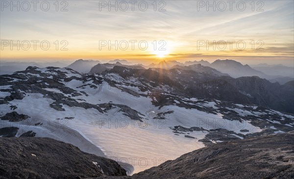 View of mountains and rocky plateau with glacier and remnants of snow at sunset