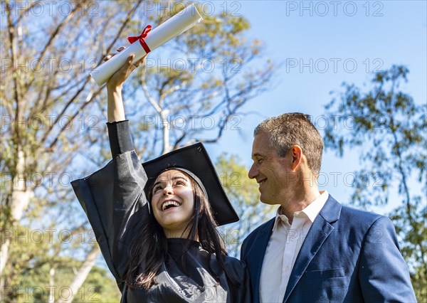 Happy graduated girl hugging her father while looking at her diploma on her graduation day