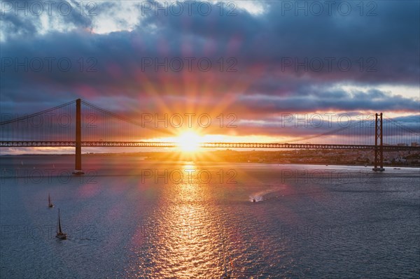 View of 25 de Abril Bridge famous tourist landmark of Lisbon connecting Lisboa and Almada on Setubal Peninsula over Tagus river with tourist yacht boats on sunset. Lisbon