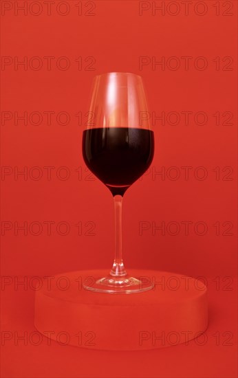 Glass of red wine on the podium. Red bright background. Minimalism. Close up. Copy space. Valentines Day concept. Mockup for holidays design
