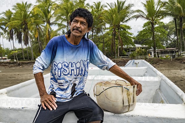 Mustached man sitting in his boat looking at the horizon. Coastal landscape of palm trees in the Central Pacific