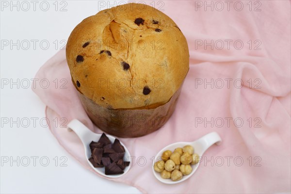 Panettone on a pink cloth and white background with ceramic spoons with hazelnuts and chocolate