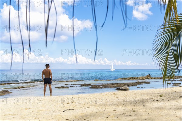 Handsome young man in barefoot swimsuit on the sandy shore