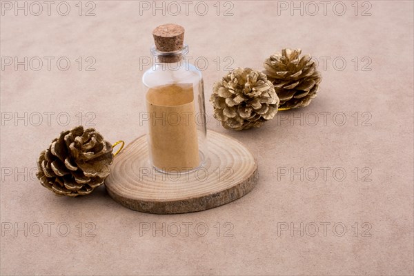 Pine cones and a bottle on a piece of cut wood on a light brown background