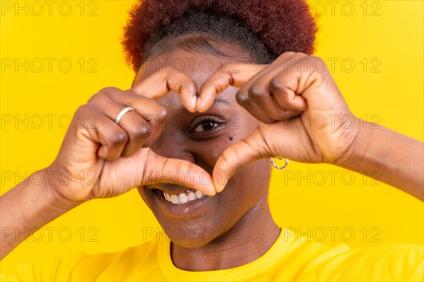 Young african american woman isolated on a yellow background smiling and heart gesture