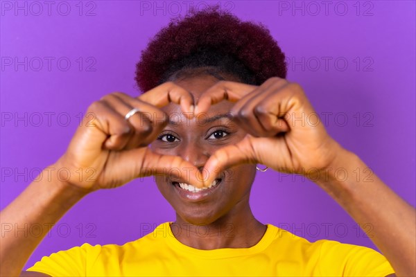 Young african american woman isolated on a purple background smiling and heart gesture