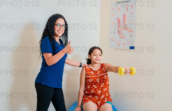 Professional physiotherapist showing thumb up while helping patient with rehabilitation dumbbells. Rehabilitation physiotherapy to patient with dumbbells