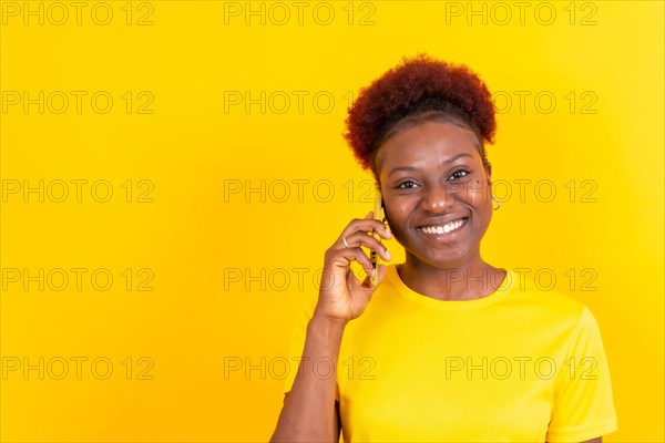 Young african american woman isolated on a yellow background smiling with the mobile phone