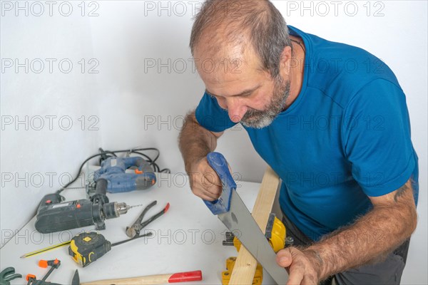 Front view of a male carpenter cutting wood in his workshop with a saw in the background with various tools on the table