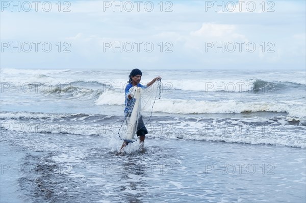 Fisherman walking with his net into the sea looking at the camera