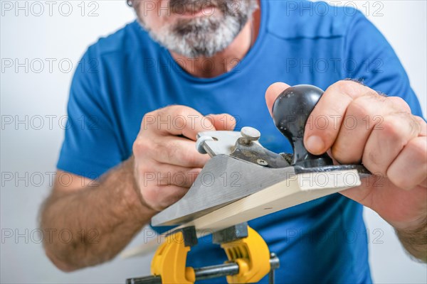 Front view of a bearded male carpenter planing wood with a hand planer isolated on white background