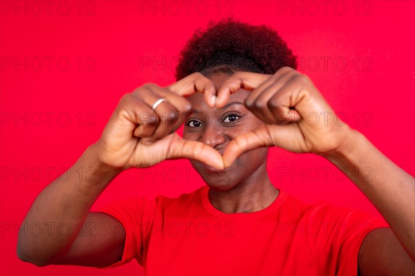 Young african american woman isolated on a red background smiling and heart gesture