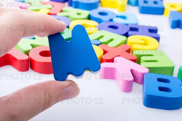 Letter M in hand beside colorful alphabet letter blocks scattered randomly