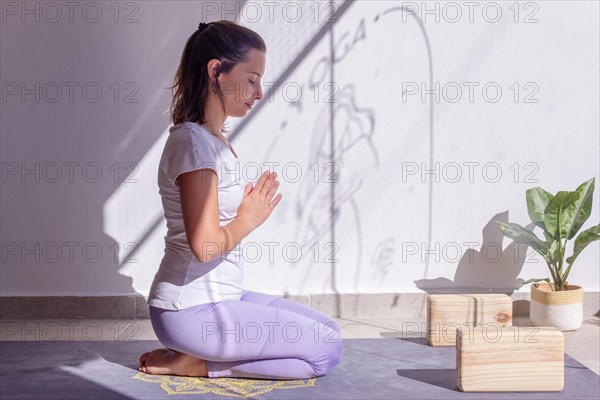 Woman meditating on her yoga mat with her hands in Anjali Mudra position in a peaceful setting with a Buddha statuette