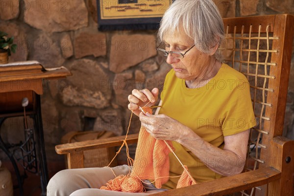 Profile portrait of an old woman concentrating on her knitting sitting in an armchair in her home