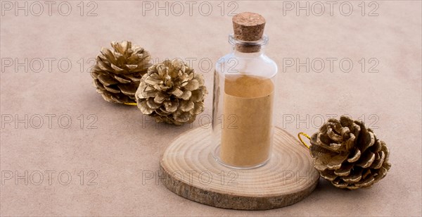 Pine cones and a bottle on a piece of cut wood on a light brown background