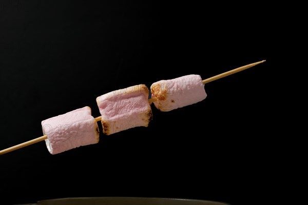 Roasted marshmallows on a skewer isolated on black background and copy space