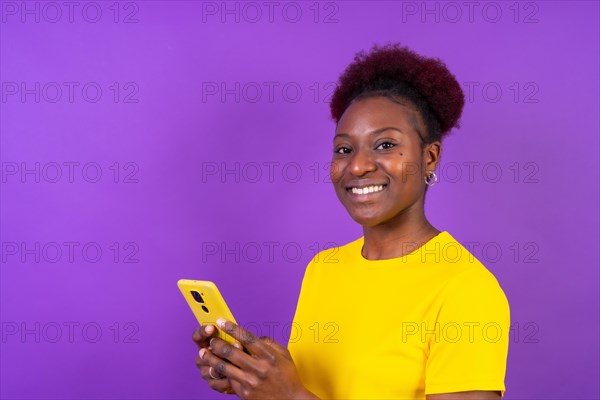 Young african american woman isolated on a purple background smiling with the mobile phone