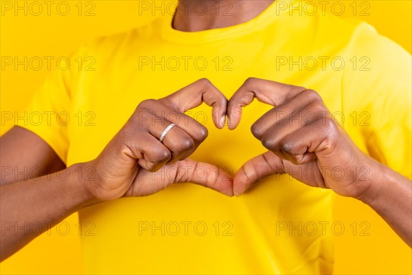 Young african american woman isolated on a yellow background smiling and heart gesture