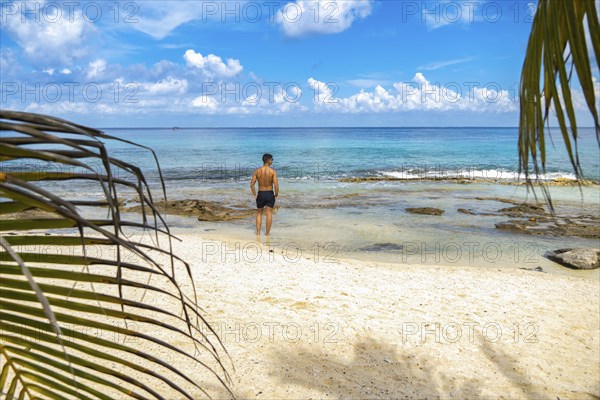 Young tourist standing barefooted on sandy coast with his back to camera