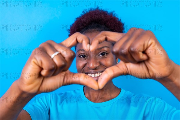 Young african american woman isolated on a blue background smiling and heart gesture