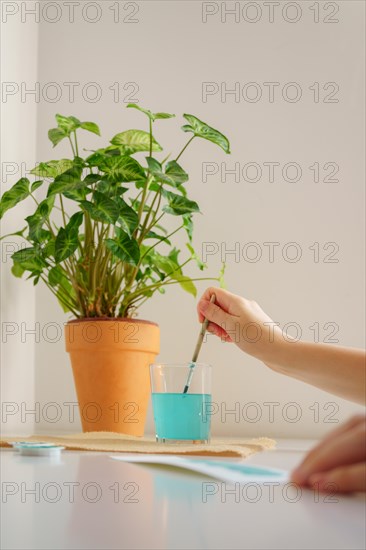 Close-up of a glass of water with a woman's hand dipping a watercolor brush in it