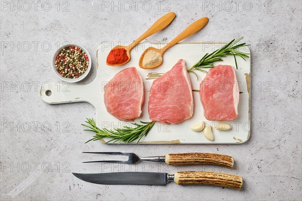 Top view of three uncooked pork cutlets on cutting board