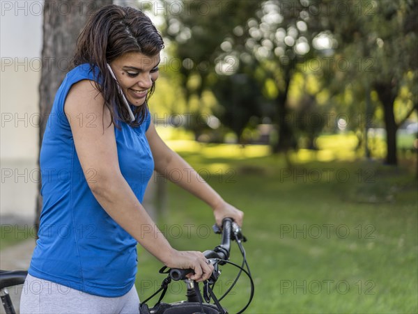 Young woman talking on her phone while pushing her bike. Copy space